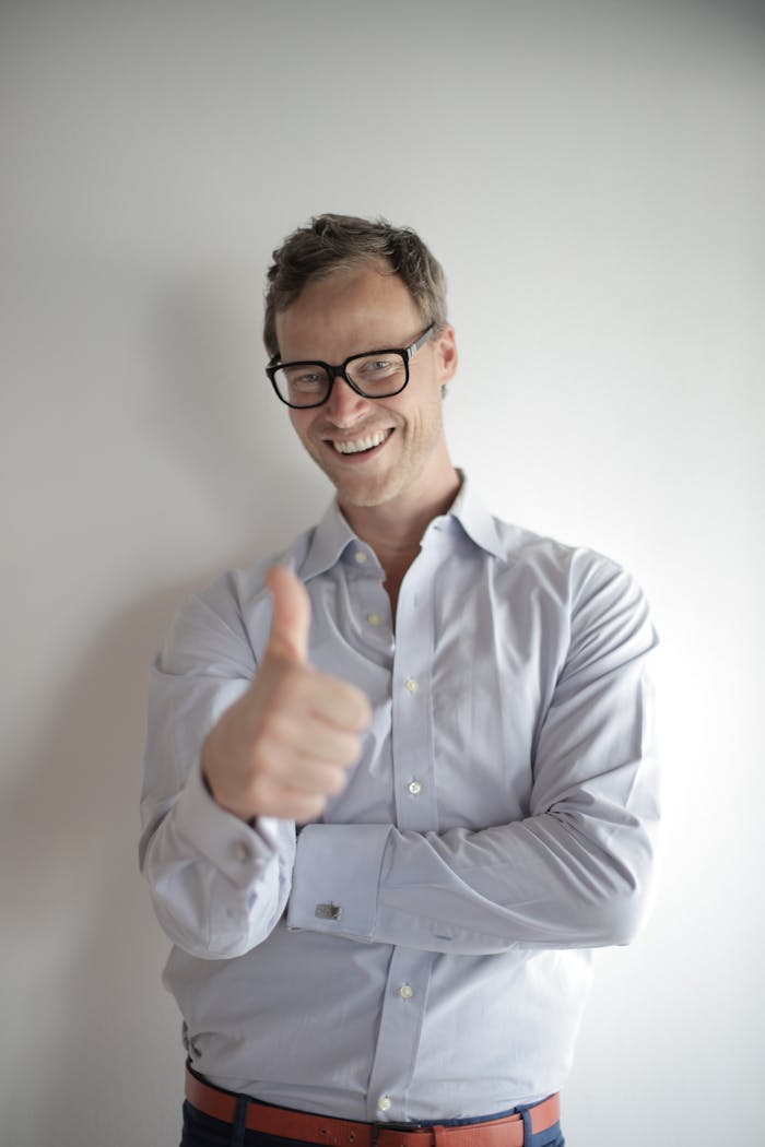 Confident young man in eyeglasses giving a thumbs up gesture, smiling against a white background.